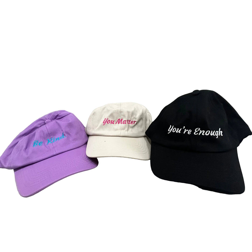 Three baseball caps with motivational phrases on a gray surface